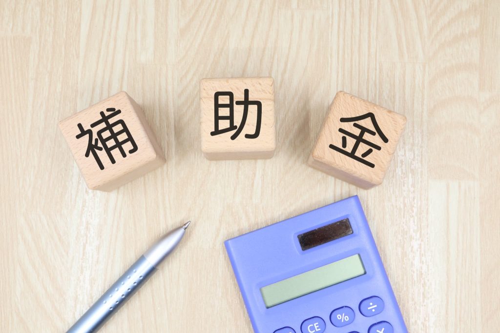 木製ブロックの補助金という文字と電卓を配置し、返済不要な資金調達方法として注目される補助金や助成金の活用イメージ