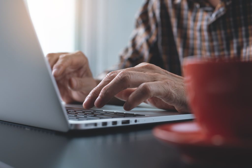 カジュアルな服装でノートパソコンを操作する男性の手元。インターネットバンキングを利用した支払いや、運転資金調達のための情報収集を行っているビジネスシーン