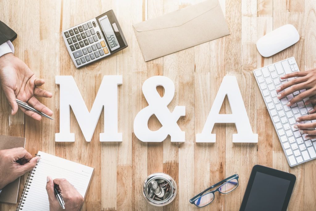 中小企業の資金調達や事業承継の手段であるM&Aという文字と、それに関連する計算や事務作業を行うデスク上の俯瞰