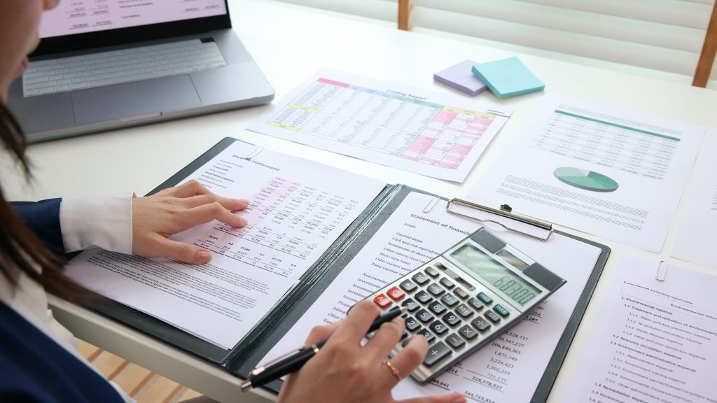 財務諸表と電卓を使い経営状況を分析しながら、自社に適した資金調達方法を検討するための計画書作成や計算を行っている手元