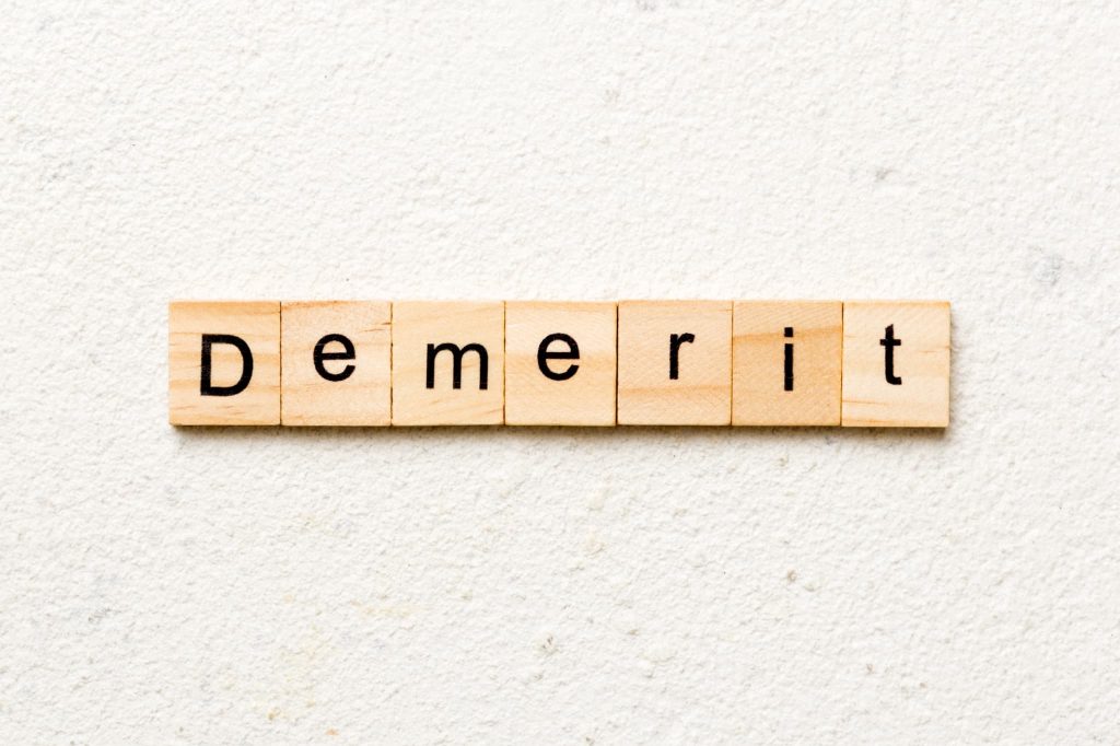 白い背景の上に並べられた「Demerit」の文字タイル。当座貸越とは便利な反面、金利や審査基準などのデメリットも存在することを示す