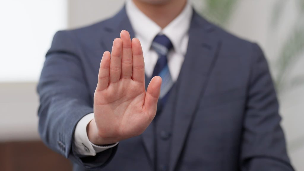 手形貸付は長年重宝されてきた便利な方法だが、2026年度末で廃止される予定という課題を想起させる、手で制止するポーズの男性