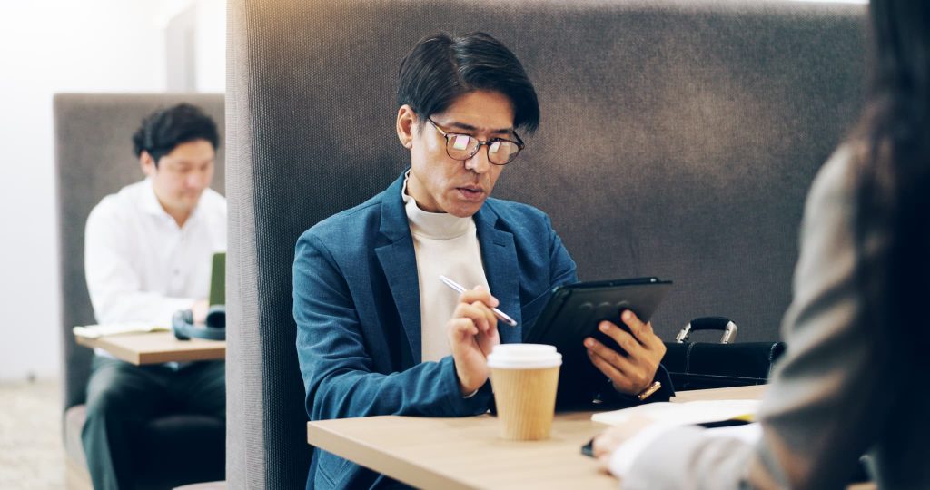 タブレット端末を使いながらコワーキングスペースで自分に適したおすすめの補助金を探している男性