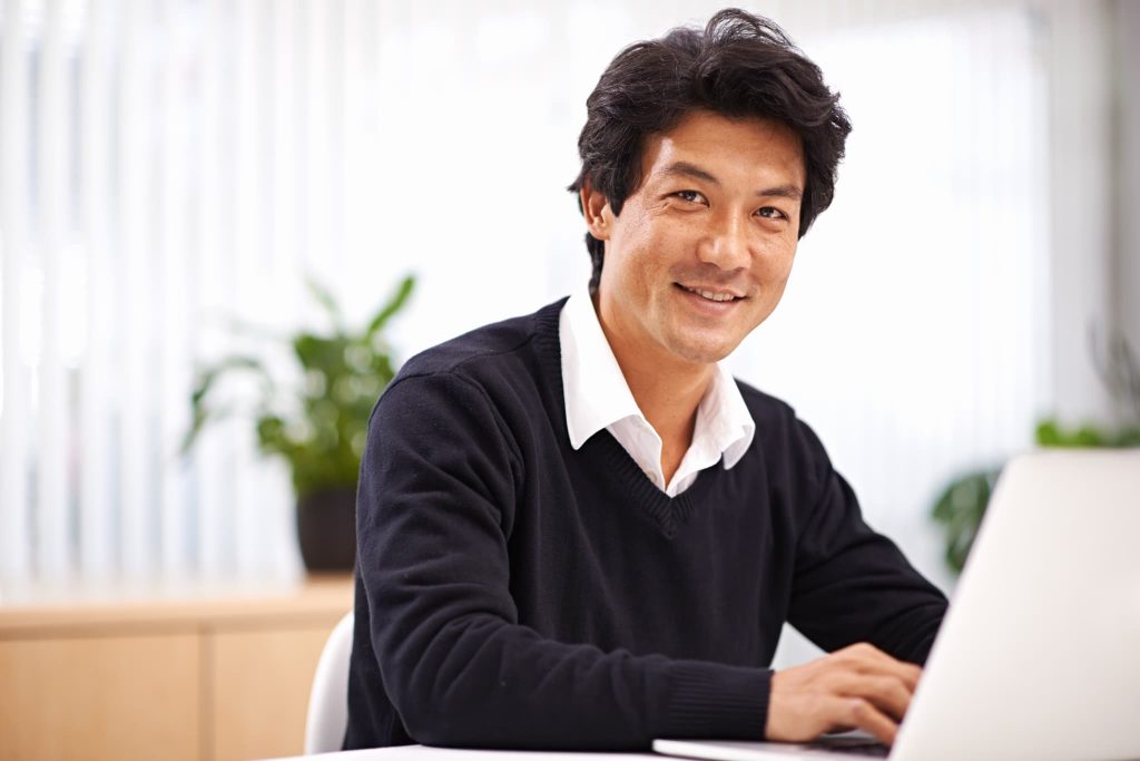パソコンの前で笑顔を見せる男性経営者。証書貸付とは企業の成長に必要なまとまった資金を調達でき経営の安定につながる資金調達手段