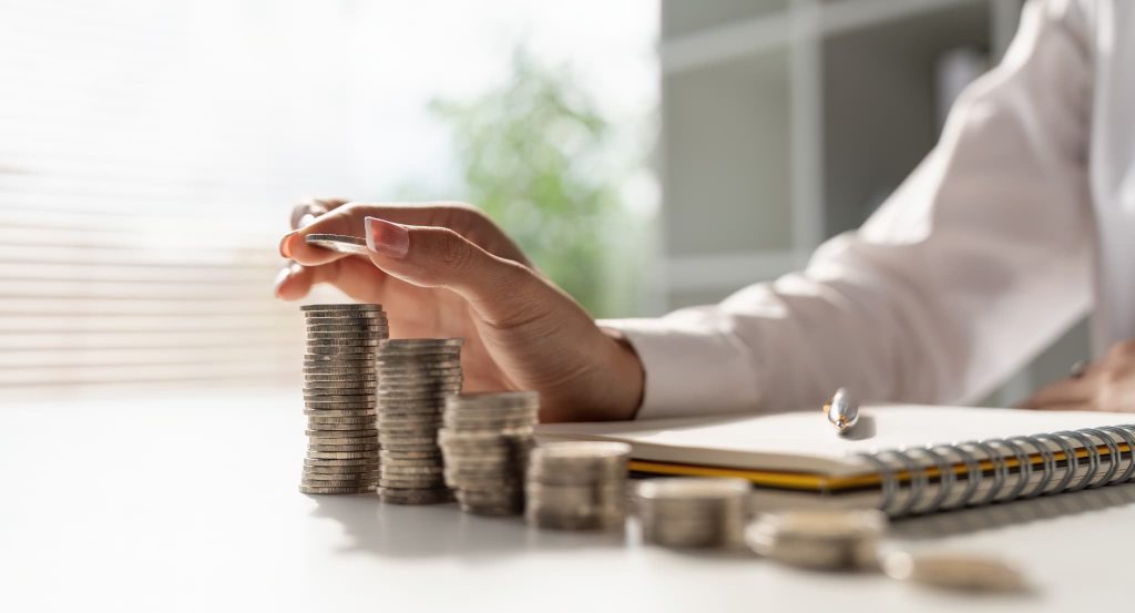 机の上で積み上げられた硬貨の高さを確認する女性の手元。美容室の運転資金を適切に管理し日々の収支バランスや利益を計算しているイメージ
