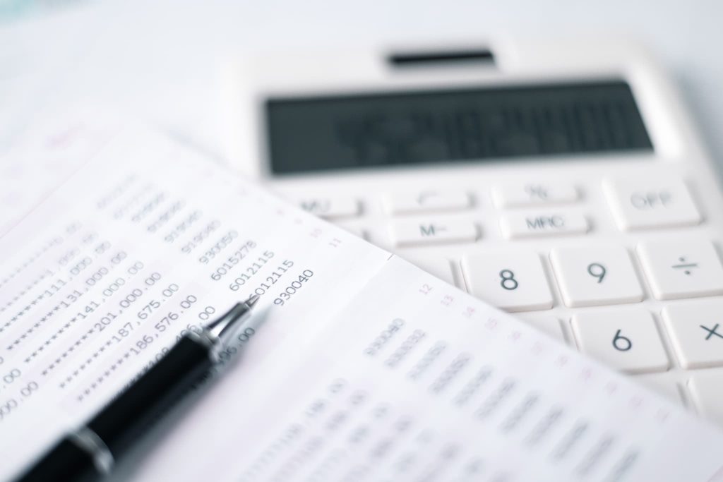 売掛金とは何かを解説する経理イメージとして、白い電卓と数字が記された通帳の上に置かれた黒いボールペン