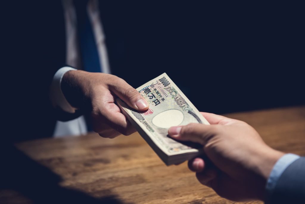 暗がりで一万円札の束を手渡している手元。ビジネスローン以外の資金調達方法のメリットとデメリットを想起させるイメージ