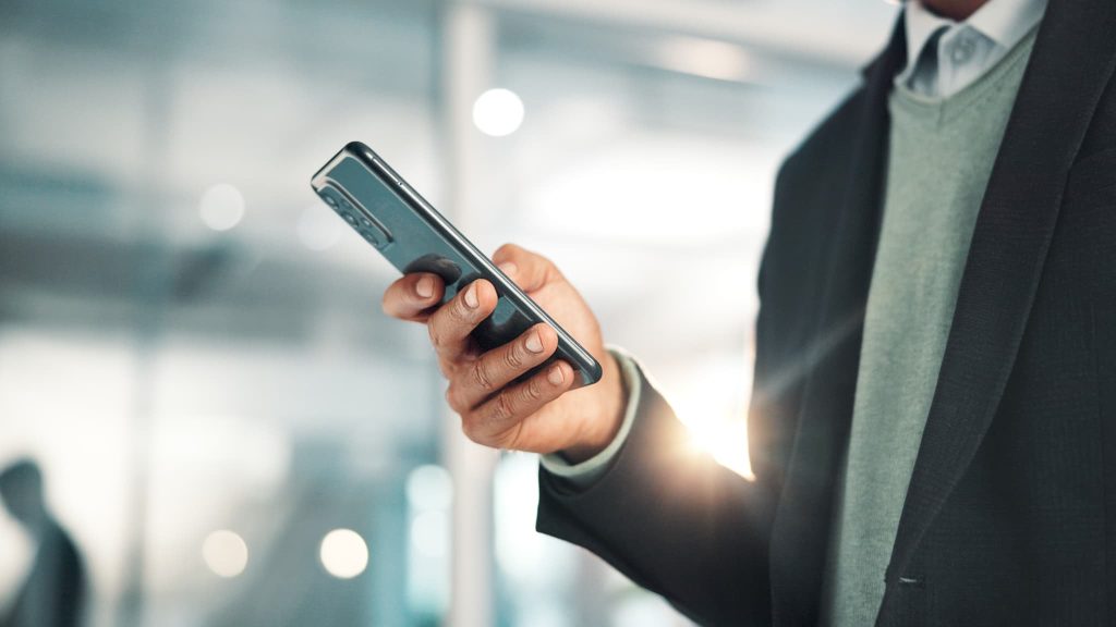 スーツを着た男性がスマートフォンを操作してファクタリングや手形割引以外の方法で資金調達の申込み連絡を行っているビジネスシーン