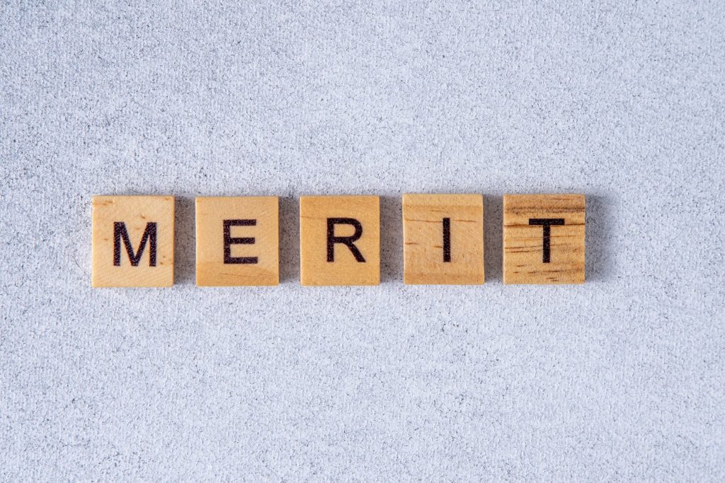MERITと書かれた木製ブロックの文字で請求書を買取に出して早期に現金化することの利点を表現