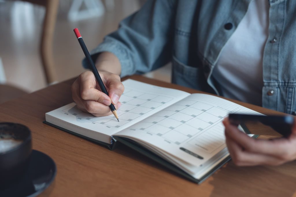 スケジュール帳のカレンダーに鉛筆で予定を書き込んでいる手元。ビジネスローンの審査にかかる日数を確認したり、即日融資を受けた後の返済期日を管理している様子