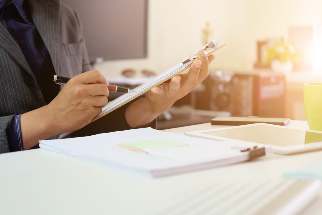 営業キャッシュフローの計算に必要な書類をクリップボードに挟み、ペンを持って内容を精査するビジネスパーソンの手元
