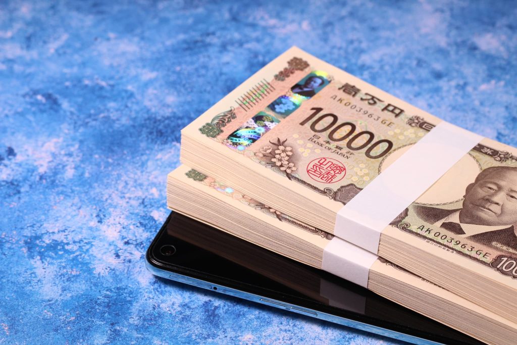 スマートフォンの上に置かれた1万円札の束。ローン審査なしのアプリ申し込みや、モバイル決済を利用したキャッシングのイメージ