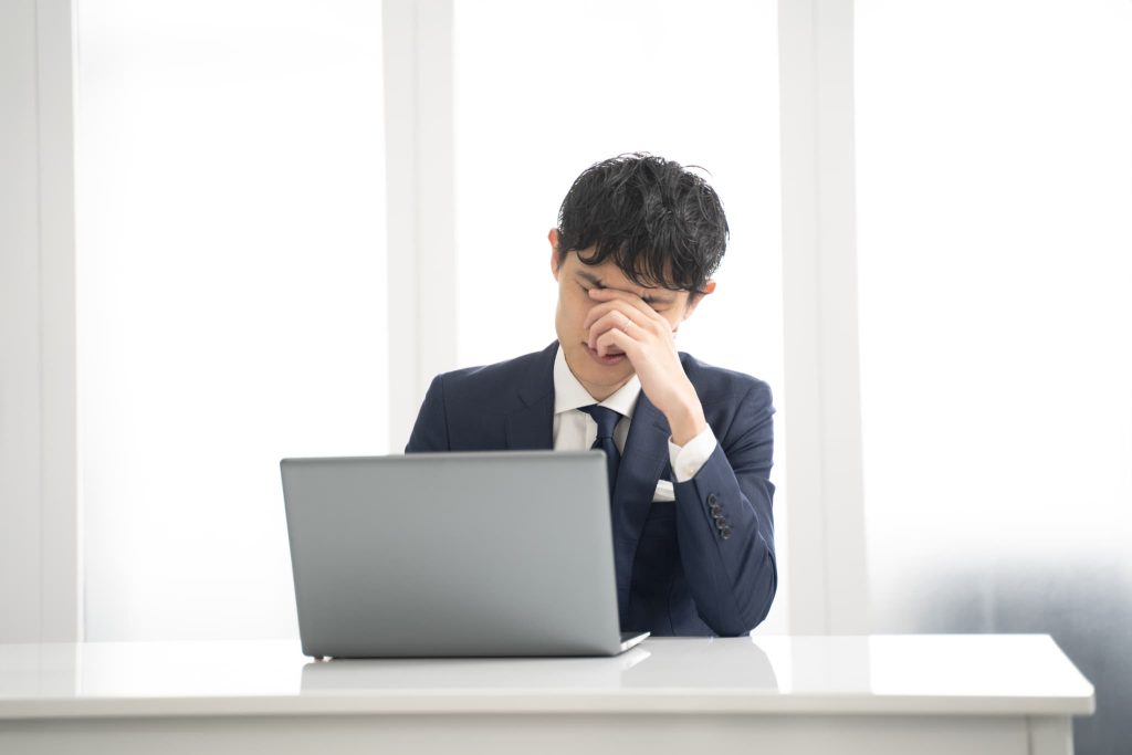 デスクでパソコンを前に頭を抱えて悩むビジネスパーソン。ローン審査なしの借入先が見つからない不安や資金繰りの苦労を想起させる