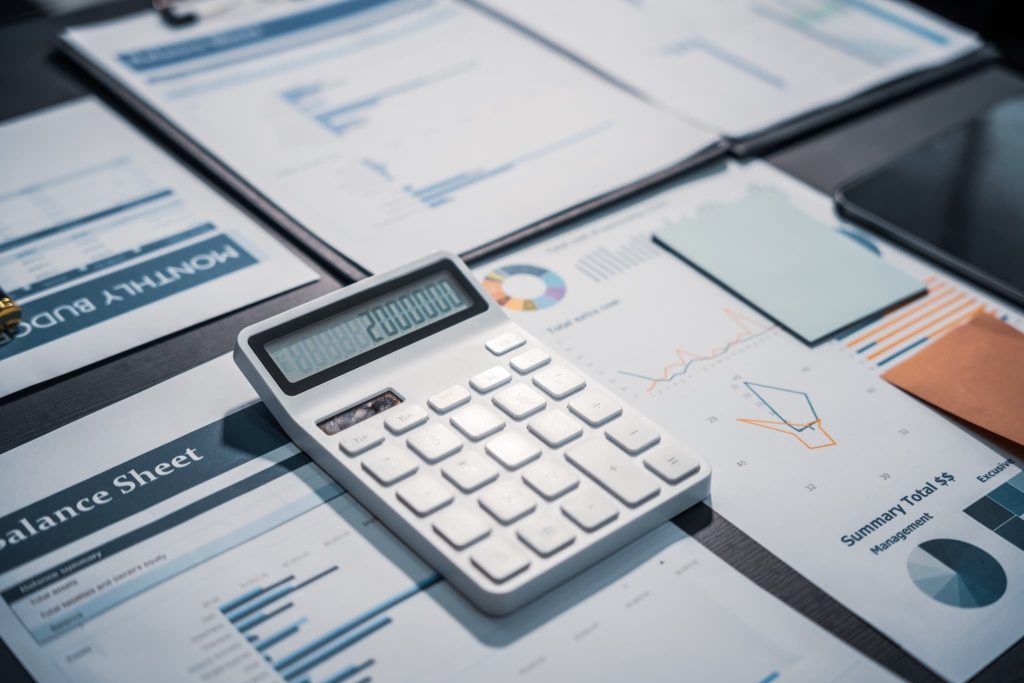 デスクに広げられた貸借対照表(Balance Sheet)などの財務書類と白い電卓。個人事業主が融資審査に向けて現在の運転資金や収支状況を計算している様子
