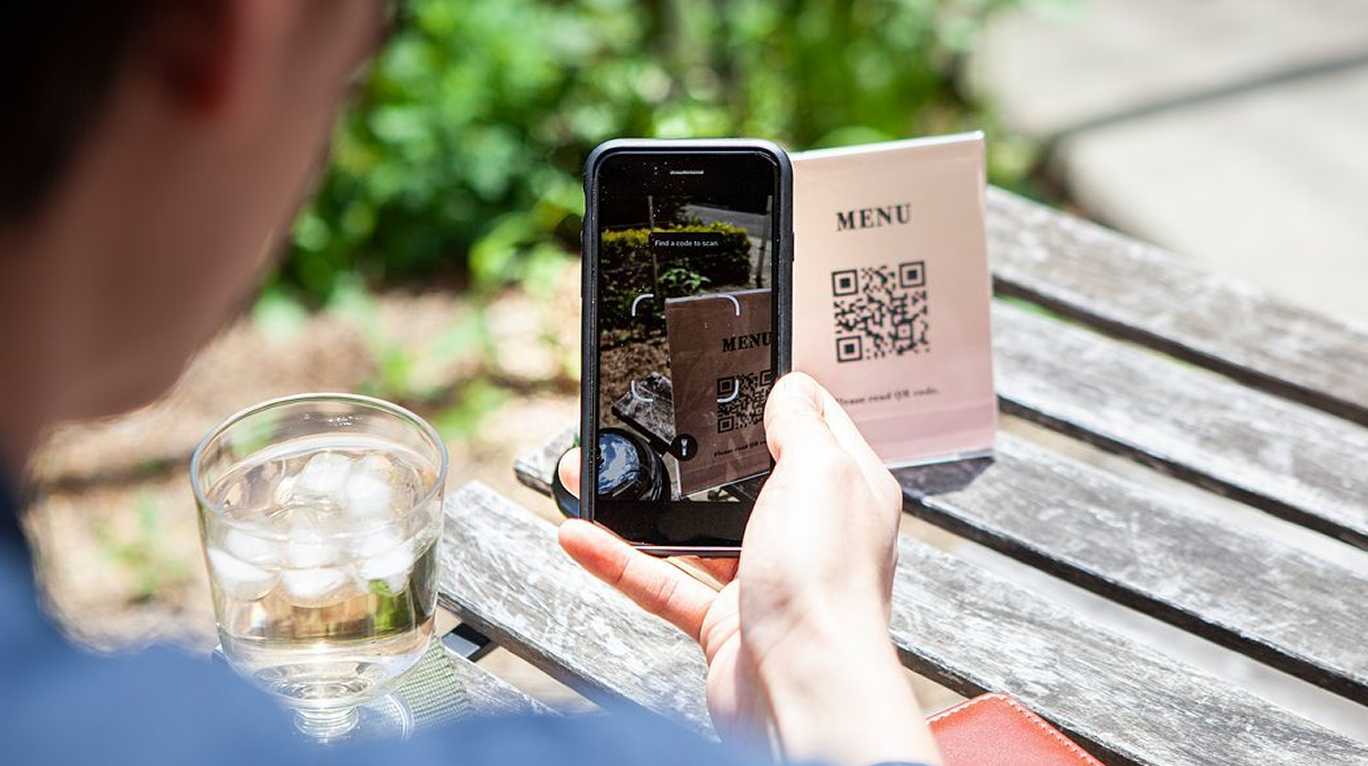 写真：カフェの席に設置されたQRをお客様が読み込んでいるシーン