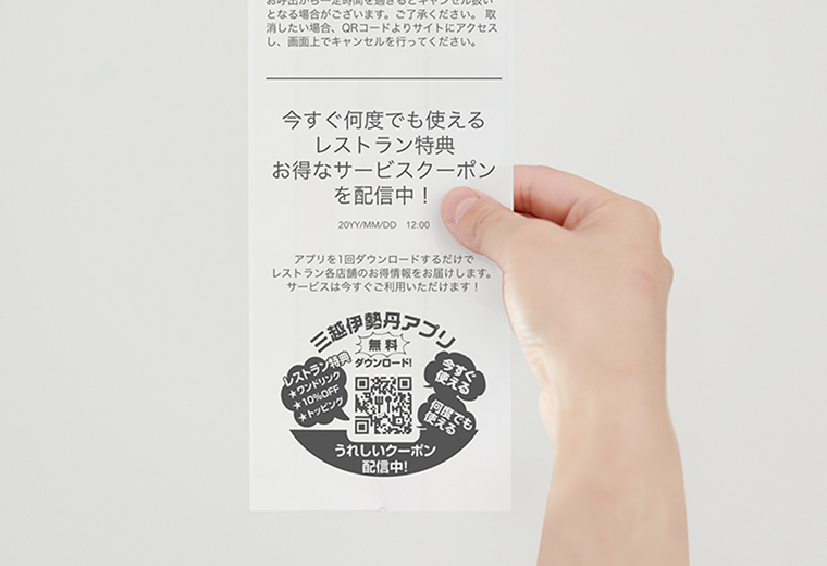 写真:クーポン券を持っている様子。クーポン券には三越伊勢丹のアプリから獲得できるクーポン情報や、アプリダウンロード用のQRなどが記載されている。